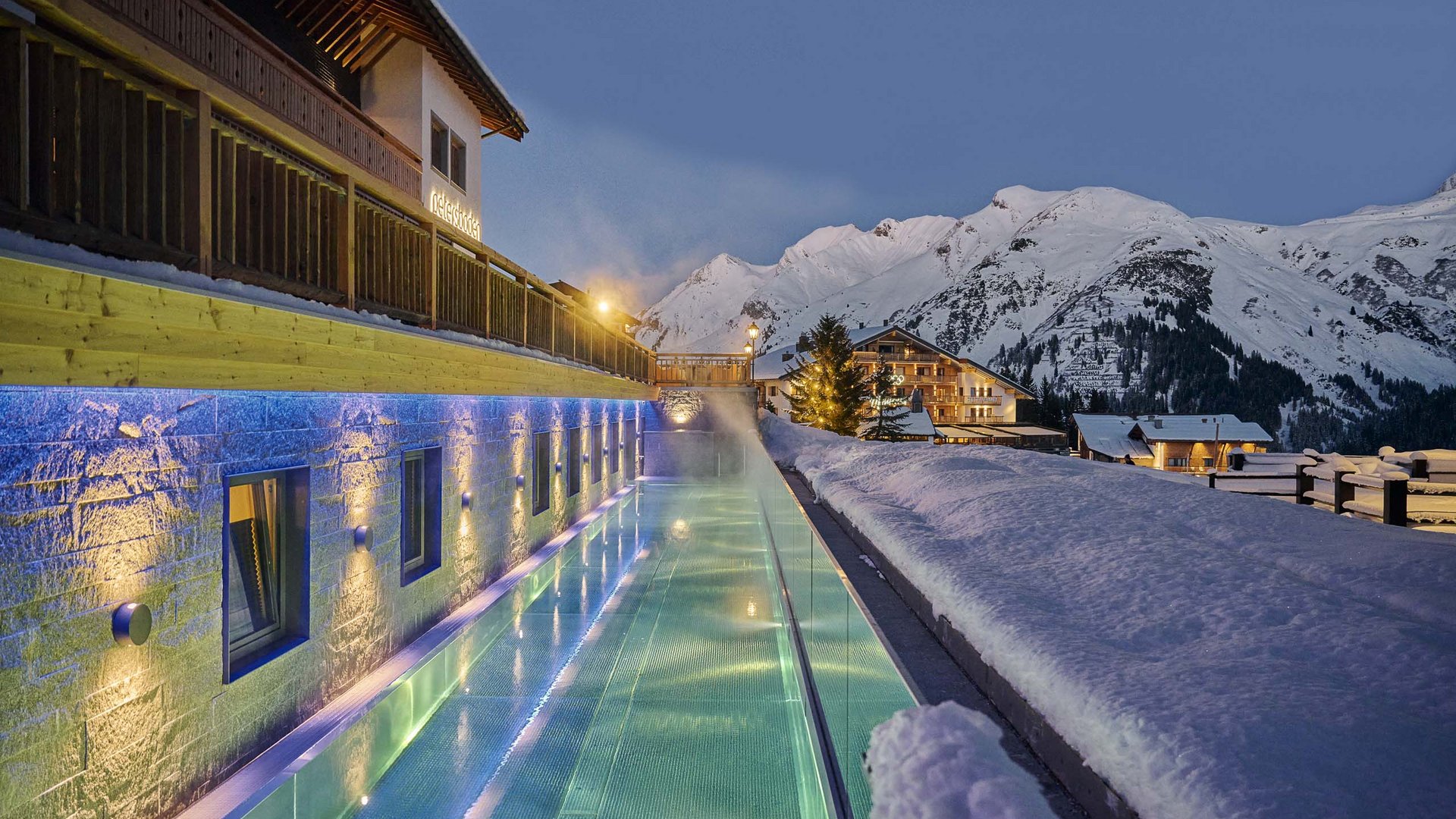 Hotel in Oberlech mit Ski-in und Ski-out, Pool und Spa Beleuchtetes Schwimmbad neben schneebedecktem Gebäude mit Alpen im Hintergrund bei Dämmerung